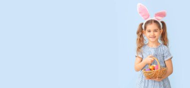 Little girl with Easter eggs and bunny ears on light background with space for text