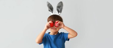 Tavşan kulaklı ve gri arka planda Paskalya yumurtaları olan sevimli küçük bir çocuk.