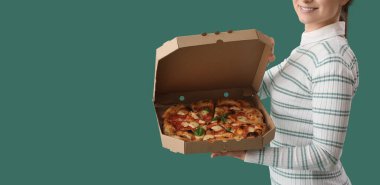 Young woman holding box with pizza on green background
