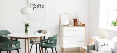 Stylish interior of light dining room with table, chest of drawers and sofa