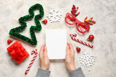 Woman holding paper sheet, gift and Christmas decor on light background