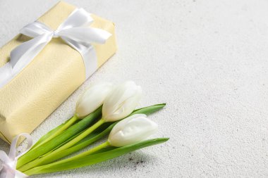 Beautiful white tulip flowers and gift box on light background