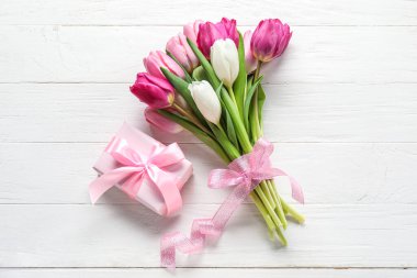 Bouquet of beautiful tulip flowers and gift box on light wooden background