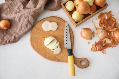 Composition with wooden board of cut onion, knife and peel on light background