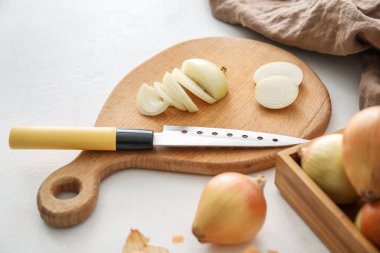 Wooden board with cut onion and knife on light background, closeup