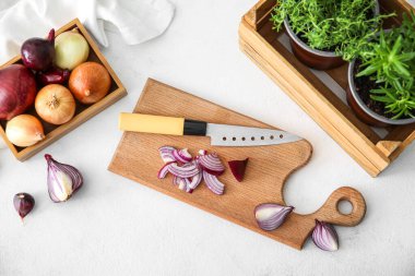 Composition with wooden board with cut onion, knife and herbs on light background