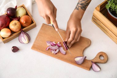 Woman cutting red onion on light background