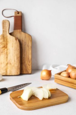 Wooden board with cut onion on light background