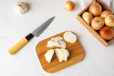Wooden board with cut onion and knife on light background