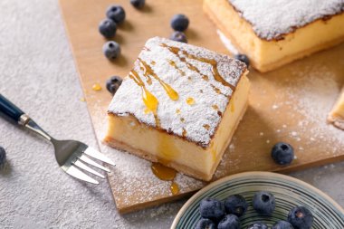 Wooden board with piece of cottage cheese casserole and blueberry on table, closeup