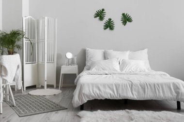 Interior of white bedroom with folding screen and palm tree