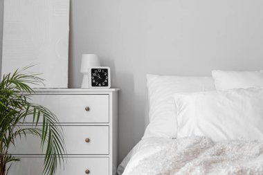 Clock with vase and painting on chest of drawers in light bedroom