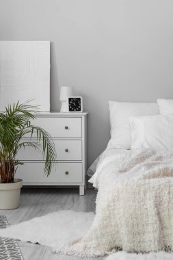 Interior of white bedroom with drawers and palm tree
