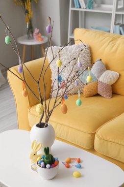 Vase with tree branches, Easter eggs, rabbits and cup on table in living room
