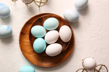 Wooden plate with beautiful Easter eggs on light background