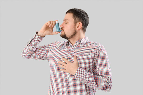 Больной человек с ингалятором на светлом фоне