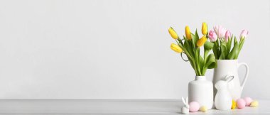 Vases with flowers, Easter eggs and toy bunnies on light background with space for text