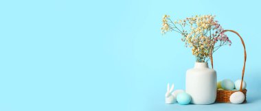 Flowers, basket of Easter eggs and toy bunny on light blue background with space for text