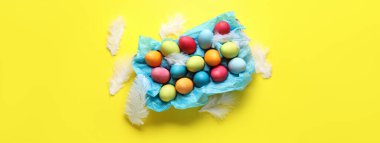 Colorful Easter eggs and feathers on yellow background