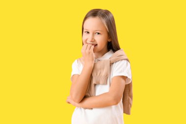 Little girl biting nails on yellow background