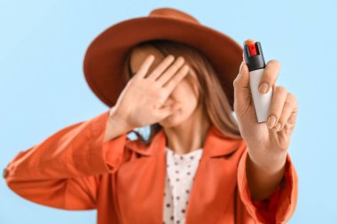 Scared young woman with pepper spray for self-defence on blue background, closeup