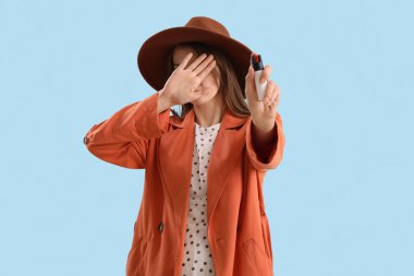 Scared young woman with pepper spray for self-defence on blue background