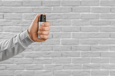 Young man with pepper spray for self-defence on grey brick background, closeup