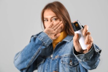 Scared young woman with pepper spray for self-defence on grey background, closeup