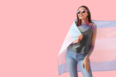 Young woman in sunglasses with transgender flag on pink background