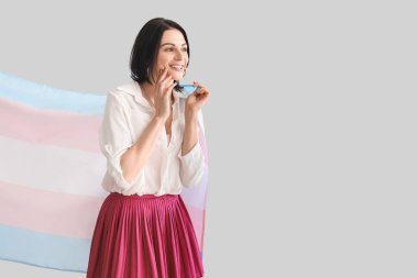 Beautiful woman with transgender flag on light background