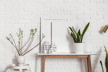 House candle holders on table and houseplants near white brick wall