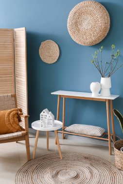 Interior of living room with house candle holders and houseplant on table near blue wall