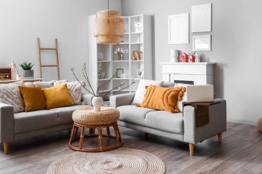 Interior of living room with sofas, houseplant and house candle holders on fireplace
