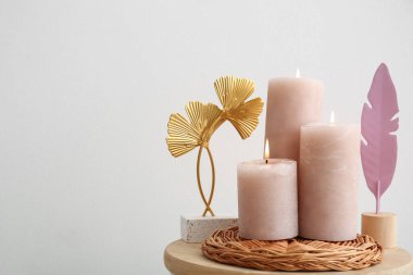 Wicker tray with burning candles and decorative feathers on table near white wall