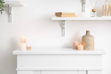 Burning candles and vase on mantelpiece in light living room