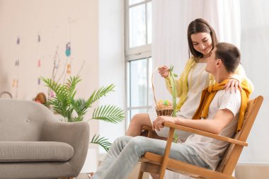 Happy young couple with basket of Easter eggs at home