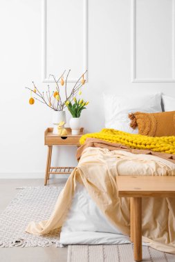 Vases with tree branches, Easter eggs, tulips and rabbit on table in bedroom