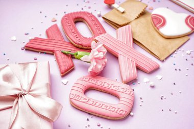 Composition with sweet cookies, gift box, paper bag and carnation flower on lilac background, closeup. Valentine's Day celebration