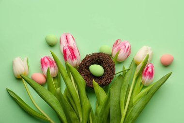 Bouquet of beautiful tulip flowers and Easter eggs on green background