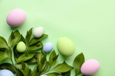 Composition with plant branches and beautiful Easter eggs on green background