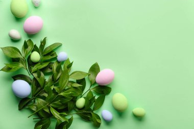 Composition with plant branches and beautiful Easter eggs on green background