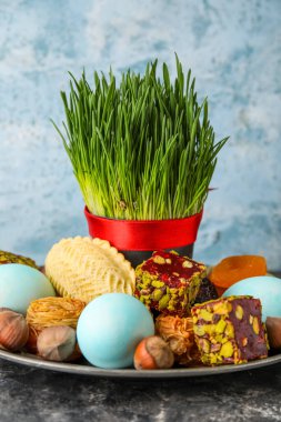 Plate with grass, eggs and treats on table near grunge wall. Novruz Bayram celebration
