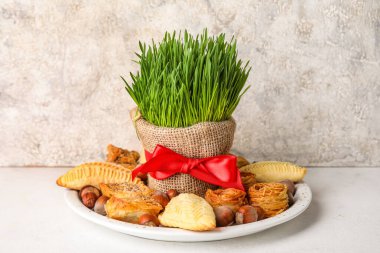 Plate with treats and grass on table near grunge wall. Novruz Bayram celebration