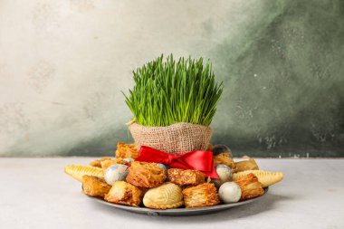 Plate with treats, eggs and grass on table near grunge wall. Novruz Bayram celebration