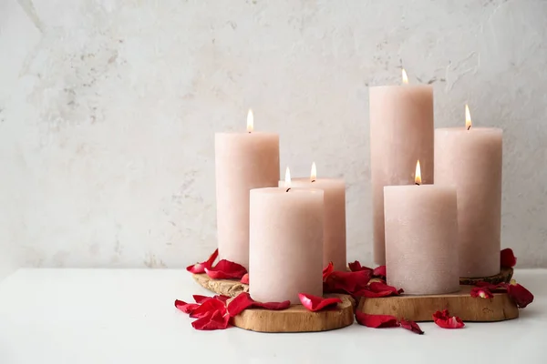 Burning candles and rose petals on white table near grunge wall, closeup