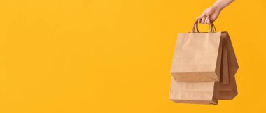 Hand holding paper shopping bags on yellow background with space for text  