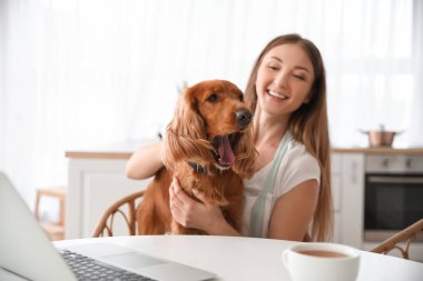 Young woman with red cocker spaniel sitting at table in kitchen