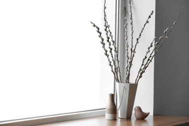 Vases with willow branches and decor on windowsill in room