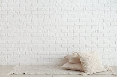 Stylish pillows on floor near light brick wall