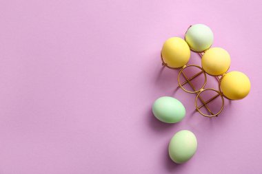 Holder with painted Easter eggs on lilac background